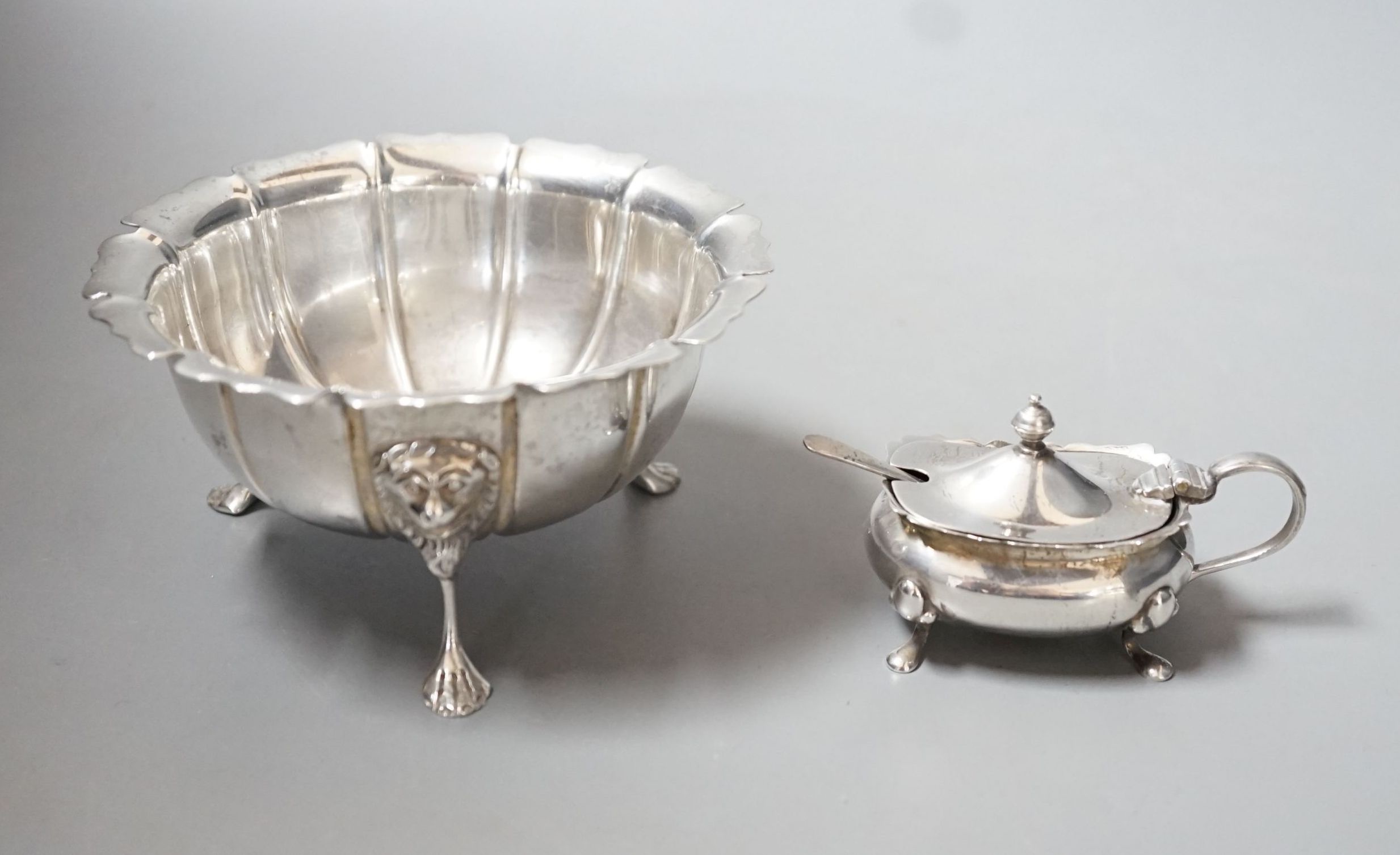 A George V Irish silver bowl, with lion mask knees on tripod supports, West & Son, Dublin, 1923, diameter 11.4cm and a silver mustard pot and spoon, 60z.